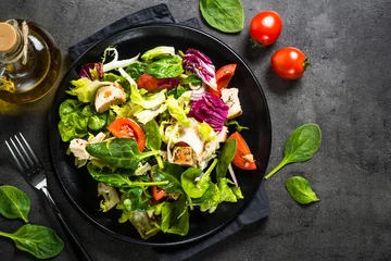 Gordijnen Green salad with chicken and vegetables on black. © nadianb