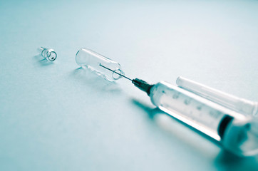 sterile syringe with a needle and an ampoule of medicine on a blue background. treatment, prevention, laboratory, infection. soft focus. copy space; mock up.