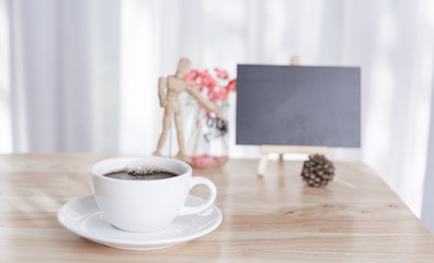 Blank black board with coffee cup and dried flower on office table with white curtain background