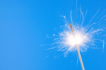 Burning christmas sparkler on blue background with room for text
