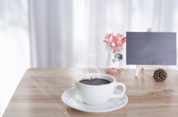 Obraz premium coffee cup with smoke and black board on office table with white curtain background in morning light
