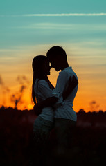 Silhouettes of happy young people hugging each other at sunset in the countryside in the evening....