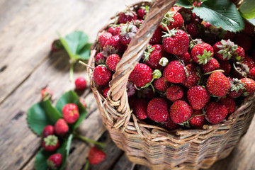 Strawberry in basket with green leaves on wooden