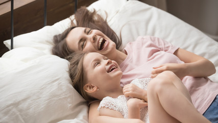 Obraz na płótnie Canvas Pretty mother and daughter lying in bed laughing having fun