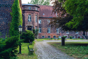 Ettal, Germany - April 17, 2019: Young redhead woman smiling into the camera sitting on a bench in the courtyard of the Benediktanerabtei Ettal