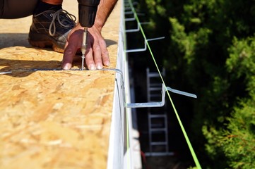 preparation of iron brackets of a roof gutter which are screwed on construction site.male Hand of...