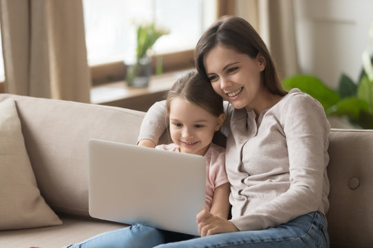 Mother with daughter sitting on couch watching movie on laptop