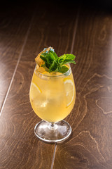 Orange Lemonade with ice cubes and mint leaves in tall glass on wooden table