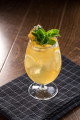 Orange Lemonade with ice cubes and mint leaves in tall glass on wooden table