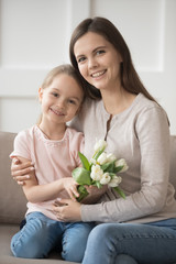 Fototapeta na wymiar Daughter holding tulips sitting with mom on couch at home