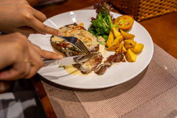 Human hand using knife and fork to eat beef steak