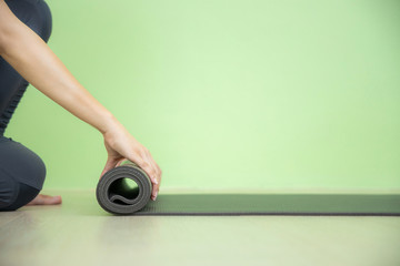 Young Asian woman concentrates on rolling black yoga mat after yoga class, close up shot.
