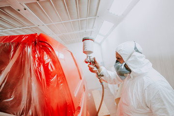 Portrait of painter working in paint booth. Mechanic painting a red car