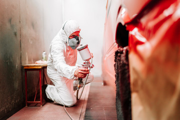 Portrait of worker with spray gun with red paint painting a car in special booth - automotive...