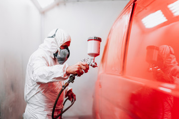 Auto manufacturing industry worker with spray gun with red paint painting a car in special booth