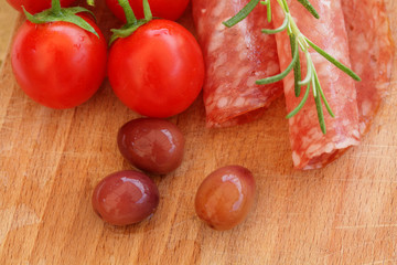 Gourmet food - salami, olives, tomatos and rosemary herbs closeup on wooden table