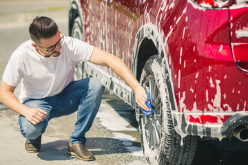 Car detailing - the man holds the microfiber in hand and polishes the car. Selective focus. Car detailing series : Worker cleaning red car. 