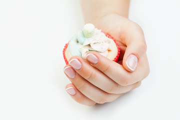 French manicured nails on female hand and cupcake on white background