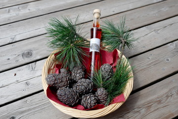 a presentation of a bottle liquor, cones and twigs from the swiss stone pine in a  wood basket