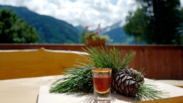 a glass liquor from the swiss stone pine, cones and twigs on a wood table with view to the mountains and of a arolla on a sunny day