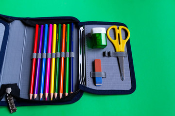Set of school supplies in a pencil case on a paper green background with copy space for text.