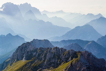 Layers of silhouettes of mountain ridges and peaks in the Italian Alps, at sunset. View from the route down from Mangart (Mangrt) peak, Julian Alps, Triglav, Slovenia.