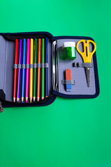School accessories, eraser, pencils, scissors, sharpener in a pencil case on a paper green background with copy space.