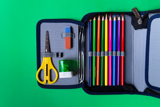 Pencil case with school supplies on a green paper background with copy space. Flat lay