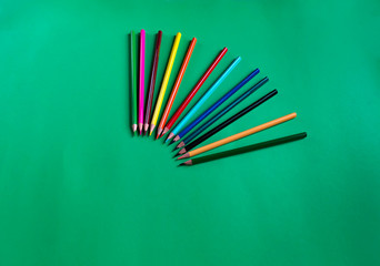 Set of multicolored wooden pencils on a green paper background with copy space. School accessory. Flat lay