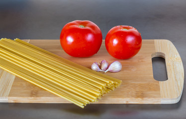 Uncooked whole wheat spaghetti pasta with tomatoes on a cutting board on a dark background.