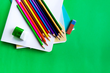 School set of notebooks, pencils, an eraser and sharpeners on a green background with copy space.