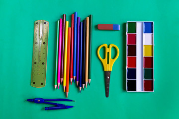 Pencils, watercolors, compasses, ruler, eraser and scissors. Set of school supplies on a green paper background with copy space. Flat lay