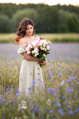 Young beautiful dark-haired girl with a bouquet of Peonies in a field of cornflowers. Summer.Cereals and field dawns. Life in the village.