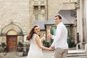 Naklejka premium Pregnant woman in dress and her husband are walking in the city. Smiling couple enjoys a walk and eats ice cream. Back view