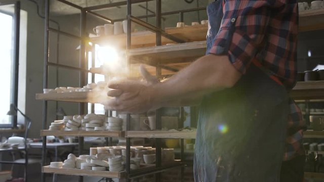 Male potter hands clapping hands on the sunlight pottery background.