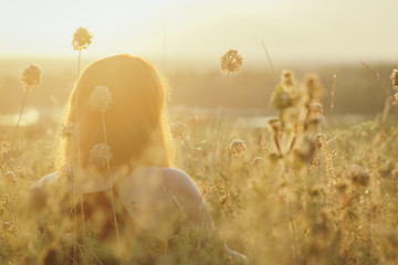 head backof red-haired girl sitting on the ground in a field among dried flowers and enjoys nature...