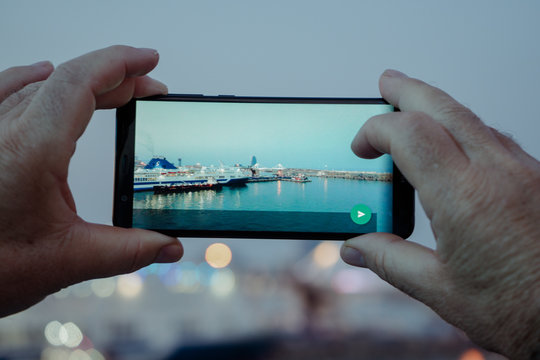 Close-up of the rear view of some hands taking photos with the mobile in a sea port at dusk