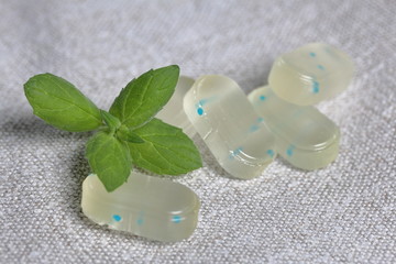 Obraz na płótnie Canvas Peppermint candies for breath freshening. With refreshing microgranules. Cooling menthol for sore throat. Nearby are fresh mint leaves. Against the background of linen fabric.