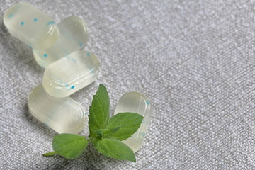 Fototapeta na wymiar Peppermint candies for breath freshening. With refreshing microgranules. Cooling menthol for sore throat. Nearby are fresh mint leaves. Against the background of linen fabric.