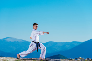 Karate man in a kimono performs a front hand kick (Choku-zuki) while standing on the green grass on...