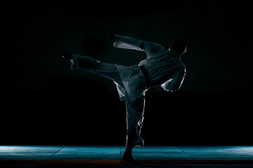 The karate silhouette guy in white kimono and black belt training karate, low key, high contrast