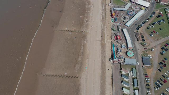 Aerial footage of the British seaside town of Hunstanton Norfolk, showing the coastal area and funfair rides with people having fun and relaxing on the beach.