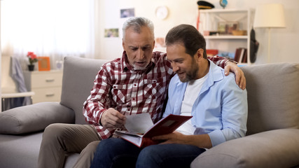 Adult father and son viewing old photos sharing good memories family traditions