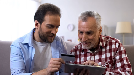 Young son and retired father inserting credit card number on tab, payment app