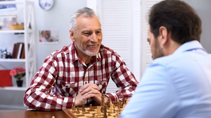 Happy senior male playing chess with son, weekend hobby and leisure activity