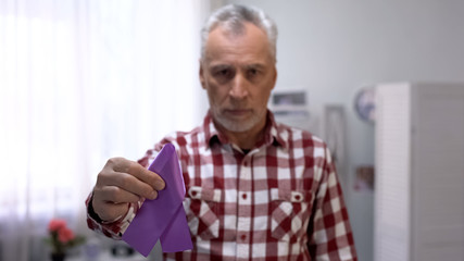 Senior male showing purple ribbon to camera, Alzheimer disease awareness, care
