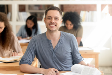 Smiling guy sitting at desk in classroom looking at camera