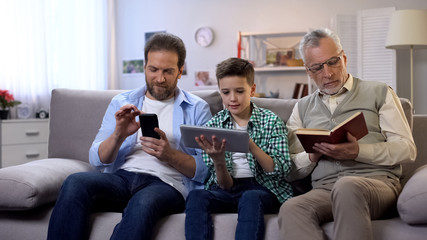 Middle-aged male and preteen boy scrolling gadgets, aging man reading paper book