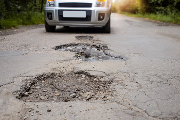 Road in terrible condition. Photo of a road with many potholes, chuckholes and driver driving the...