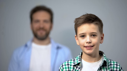 Obraz premium Boy smiling at camera, father standing on background, family care and support